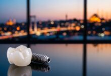 Un implant dentaire en titane et sa couronne en zircone posés sur une surface réfléchissante, avec en arrière-plan flou la ville d'Istanbul au crépuscule.
