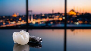 Un implant dentaire en titane et sa couronne en zircone posés sur une surface réfléchissante, avec en arrière-plan flou la ville d'Istanbul au crépuscule.