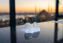 Primo piano di una faccetta dentale in ceramica bianca e perfetta, appoggiata su un tavolo lucido. Sullo sfondo, una vista sfocata e suggestiva dello skyline di Istanbul al tramonto, a rappresentare il turismo dentale di alta qualità in Turchia.
