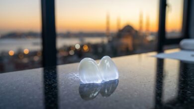 Primo piano di una faccetta dentale in ceramica bianca e perfetta, appoggiata su un tavolo lucido. Sullo sfondo, una vista sfocata e suggestiva dello skyline di Istanbul al tramonto, a rappresentare il turismo dentale di alta qualità in Turchia.