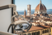 Vue composite d'une clinique dentaire moderne et d'un paysage urbain italien ensoleillé. Au premier plan, des équipements dentaires high-tech légèrement flous dans un environnement stérile. En arrière-plan, une place historique ou une ville côtière italienne baignée de lumière chaude, montrant l'alliance des soins dentaires et du tourisme en Italie, sans aucun texte.