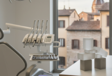 Interno di uno studio dentistico moderno e luminoso in Italia, con strumenti odontoiatrici sterili in primo piano e una pila di blocchi astratti che simboleggiano la pianificazione finanziaria su una scrivania. Sullo sfondo sfocato si intravede una classica città italiana, a rappresentare la trasparenza sui costi delle cure dentali.