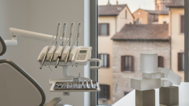 Interno di uno studio dentistico moderno e luminoso in Italia, con strumenti odontoiatrici sterili in primo piano e una pila di blocchi astratti che simboleggiano la pianificazione finanziaria su una scrivania. Sullo sfondo sfocato si intravede una classica città italiana, a rappresentare la trasparenza sui costi delle cure dentali.