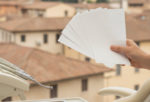 Un primo piano di una mano che tiene documenti finanziari astratti su uno sfondo sfocato di attrezzature dentali moderne e un paesaggio urbano italiano.