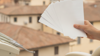 Un primo piano di una mano che tiene documenti finanziari astratti su uno sfondo sfocato di attrezzature dentali moderne e un paesaggio urbano italiano.